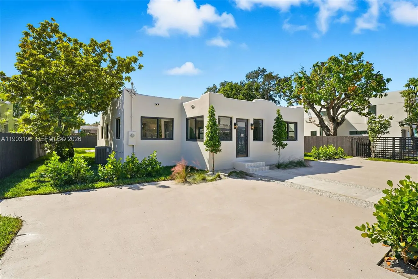A white, one-story house with black trim, a black door, and a concrete driveway on a sunny day.