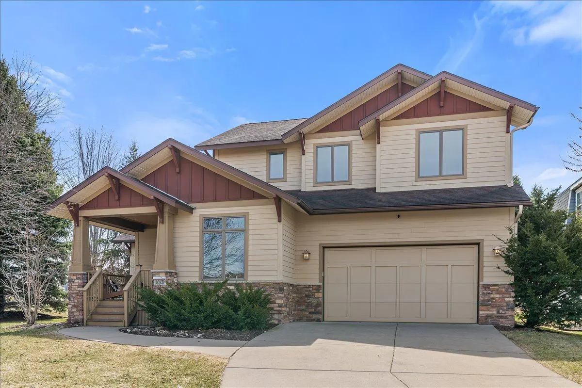 Two-story beige house with a brown roof and a two-car garage on a sunny day.