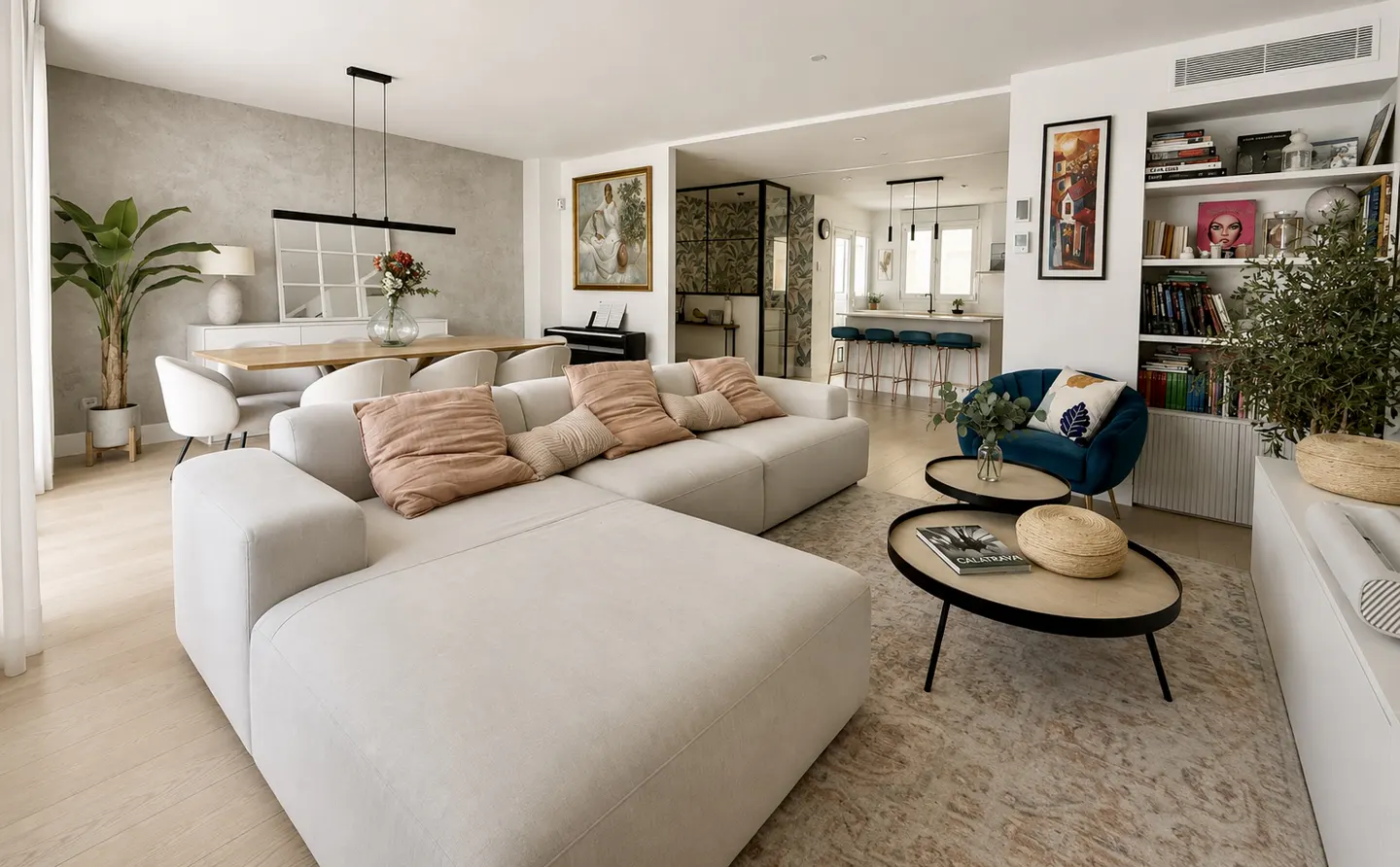 Bright, open-concept living space with a large, light-beige sectional sofa, dining table, and kitchen in the background.
