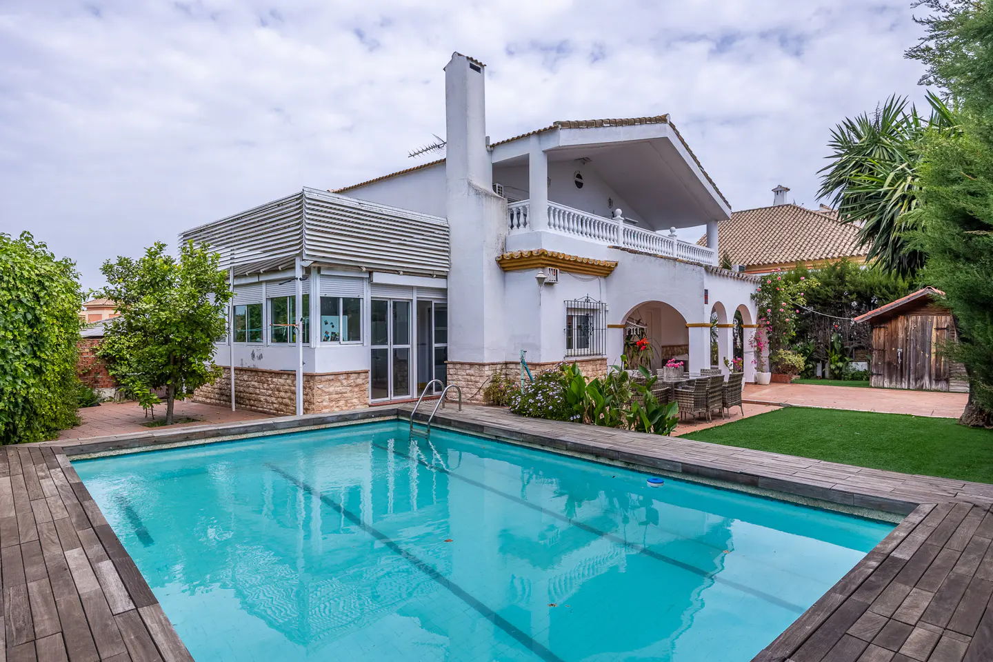 A white two-story house with a pool and wooden deck on a cloudy day.