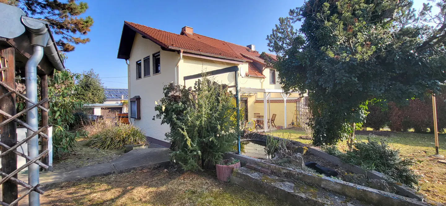 Two-story yellow house with a red tile roof, seen from the backyard with a pond and patio.