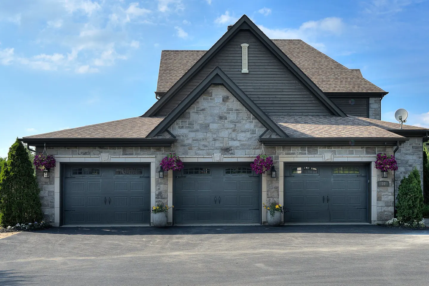 Three-car garage with gray doors and stone facade. Hanging flower baskets add color. Blue sky background.
