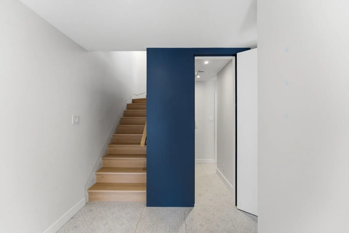 Interior view of a home featuring light wood stairs, a blue accent wall, and a doorway with a white door.