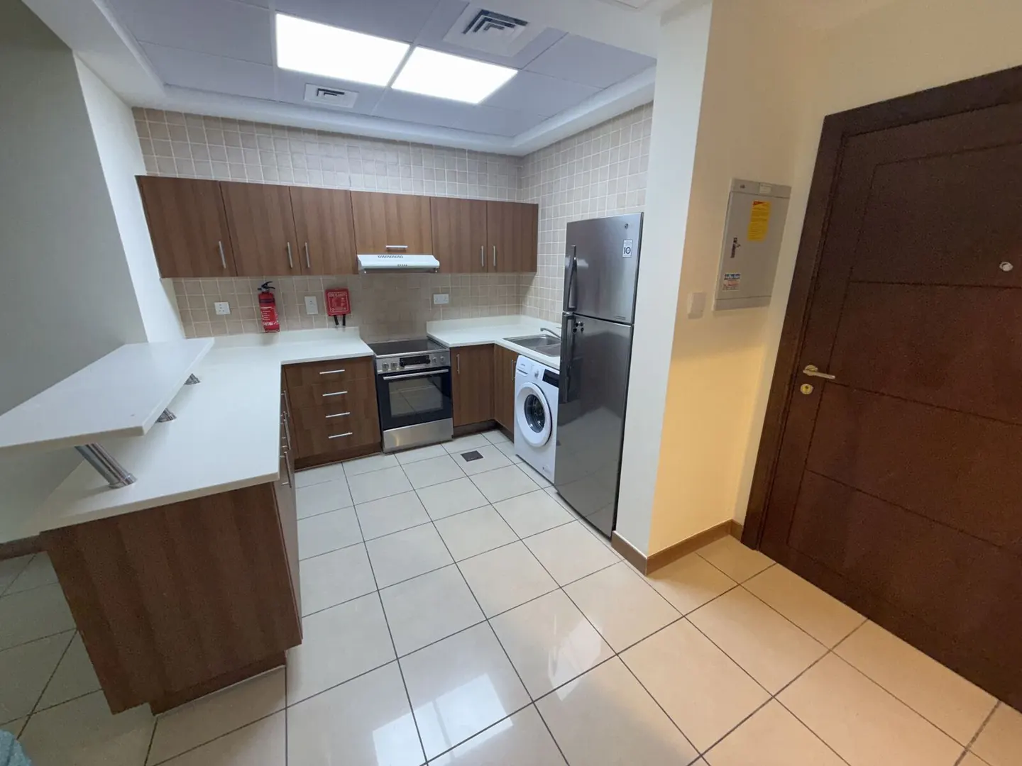 A bright kitchen with brown cabinets, white countertops, stainless steel appliances, and a washing machine.