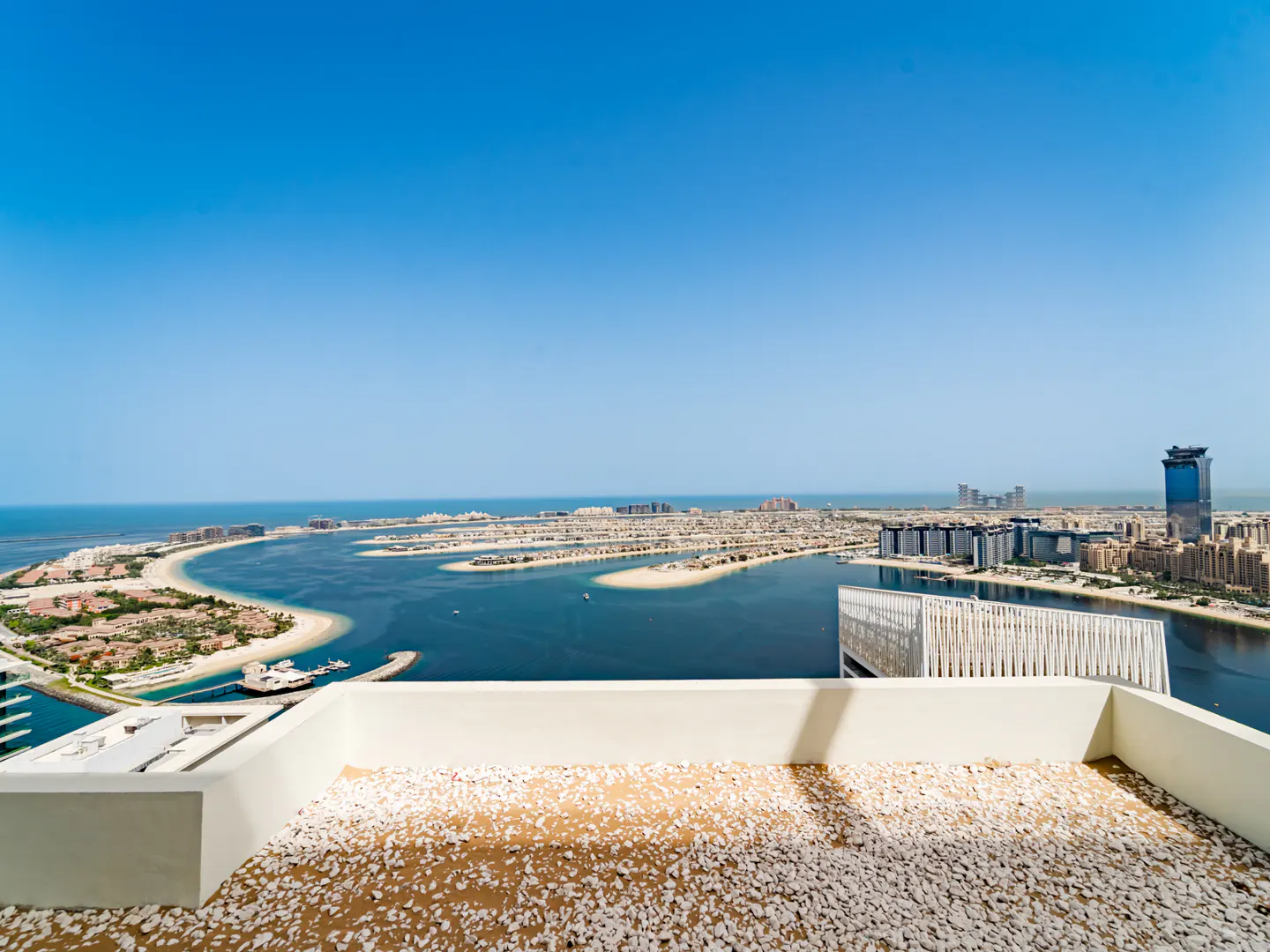 High-angle view from a white balcony with gravel flooring overlooking the Palm Jumeirah islands and the blue ocean.