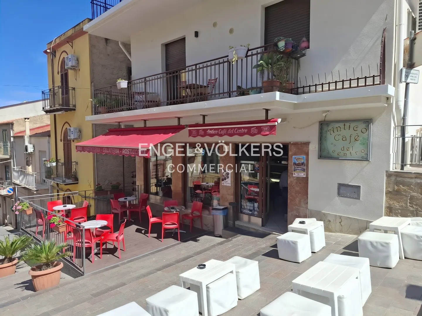 Outdoor cafe with red chairs and white tables. "Antico Cafe del Centro" sign is visible. Balcony with plants above.