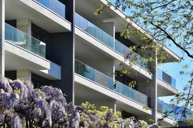 Modern apartment building with glass balconies and blooming wisteria in the foreground.