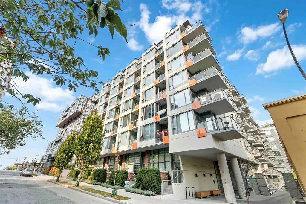 Exterior view of a modern, multi-story condo building with balconies, large windows, and gray facade, under a blue sky with scattered clouds.
