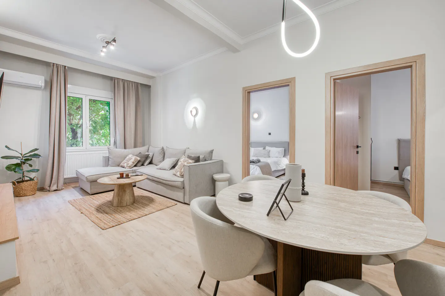 Bright living room with a gray sectional sofa, round table, and two doorways leading to bedrooms.