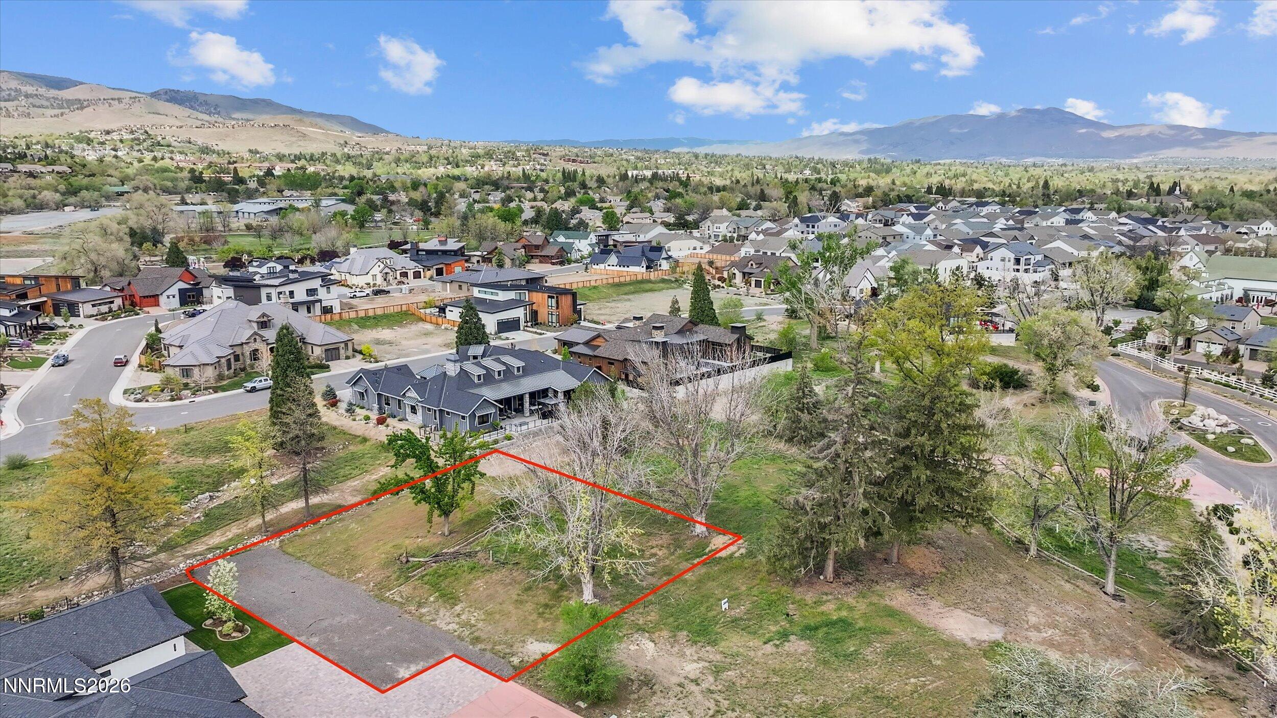 Aerial view of a vacant lot outlined in red, surrounded by houses and trees, with mountains in the background.
