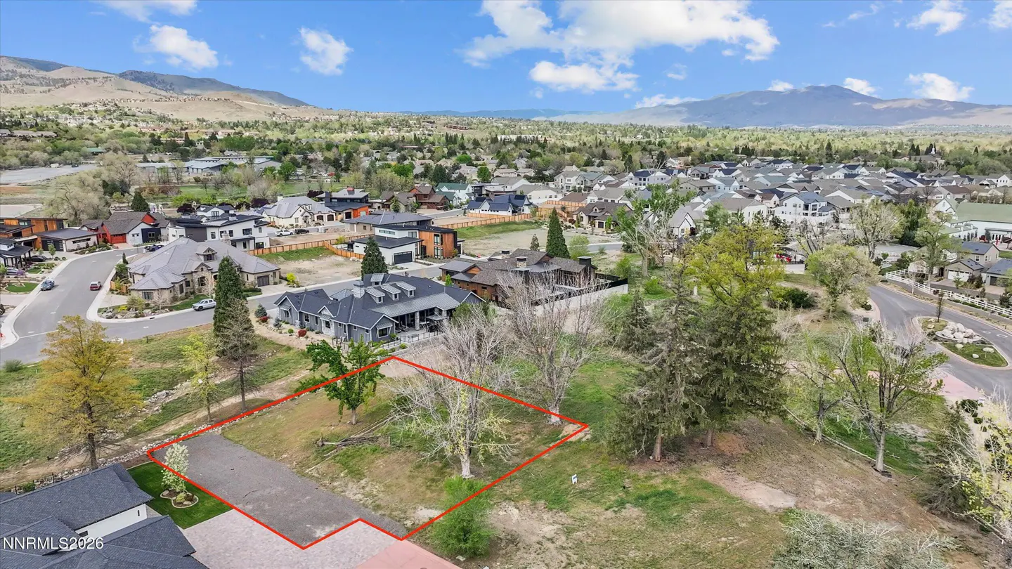 Aerial view of a vacant lot outlined in red, surrounded by houses and trees, with mountains in the background.