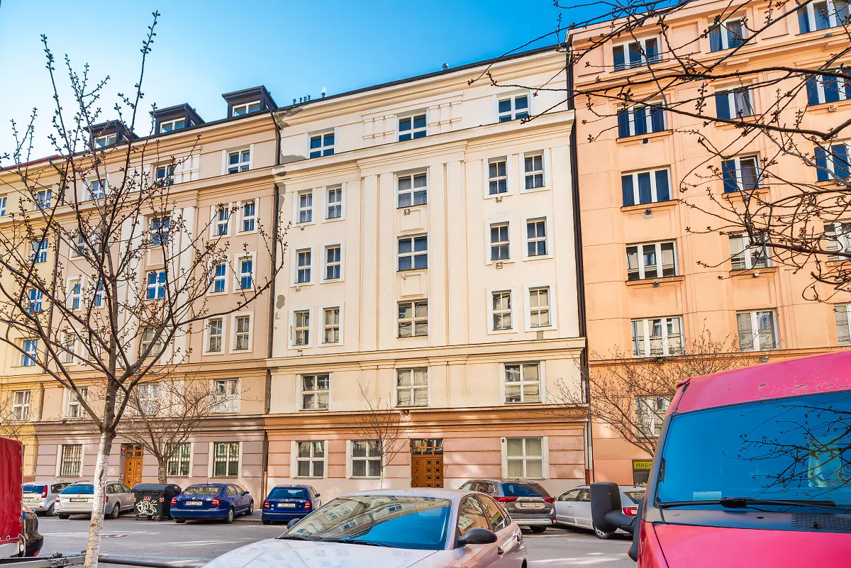 Street view of multi-story apartment buildings in shades of beige and peach with parked cars in the foreground.