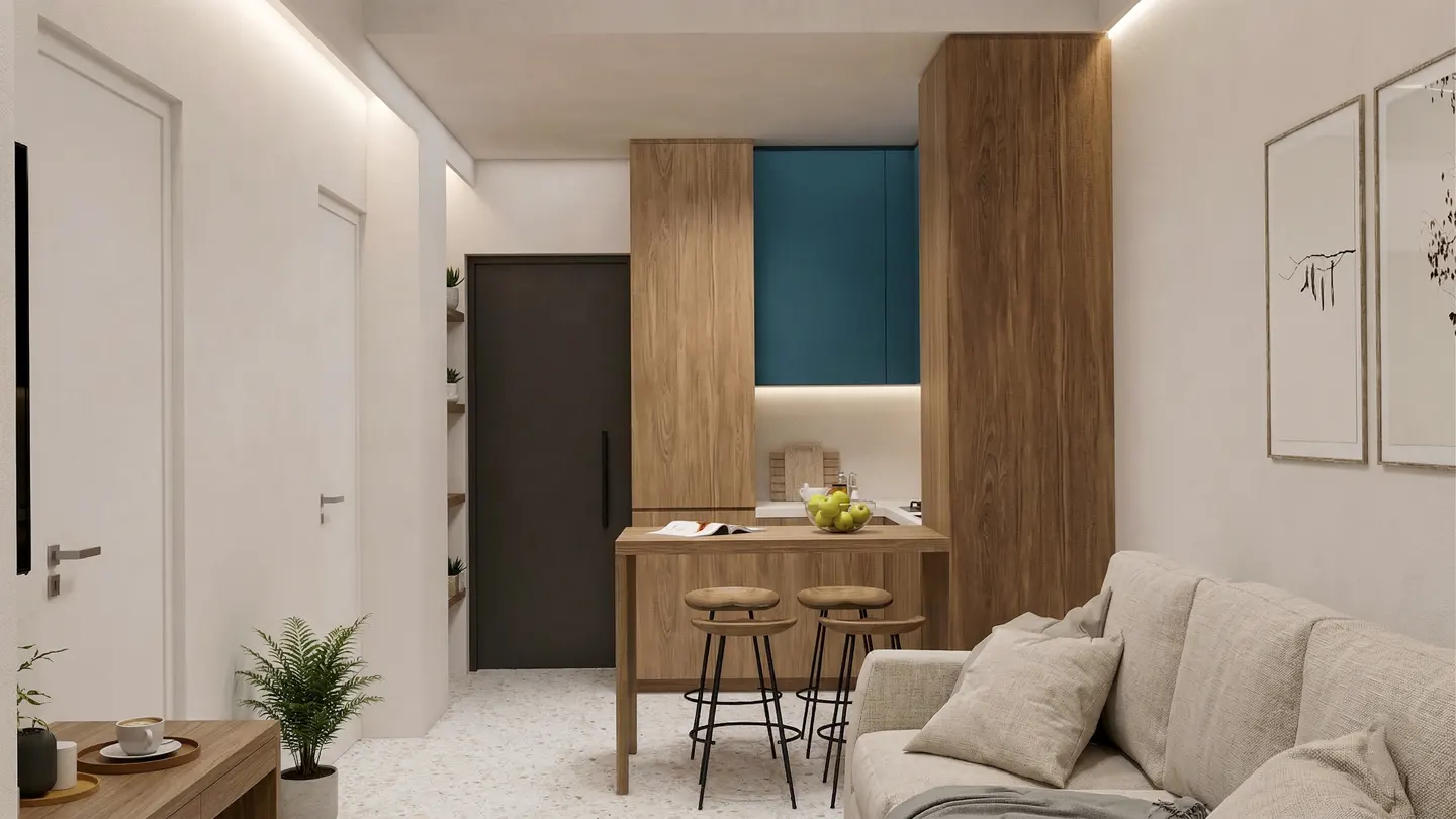 Interior view of a modern apartment with a beige sofa, wooden bar table with stools, and blue kitchen cabinets.