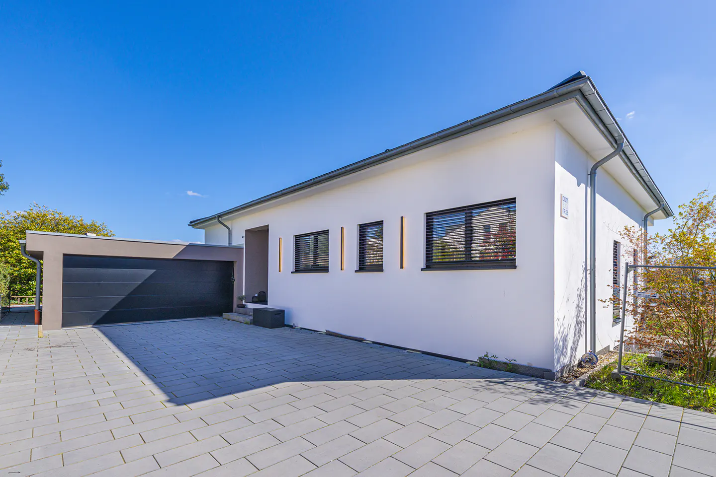Modern white house with a dark gray garage under a clear blue sky. The driveway is paved with gray stones.