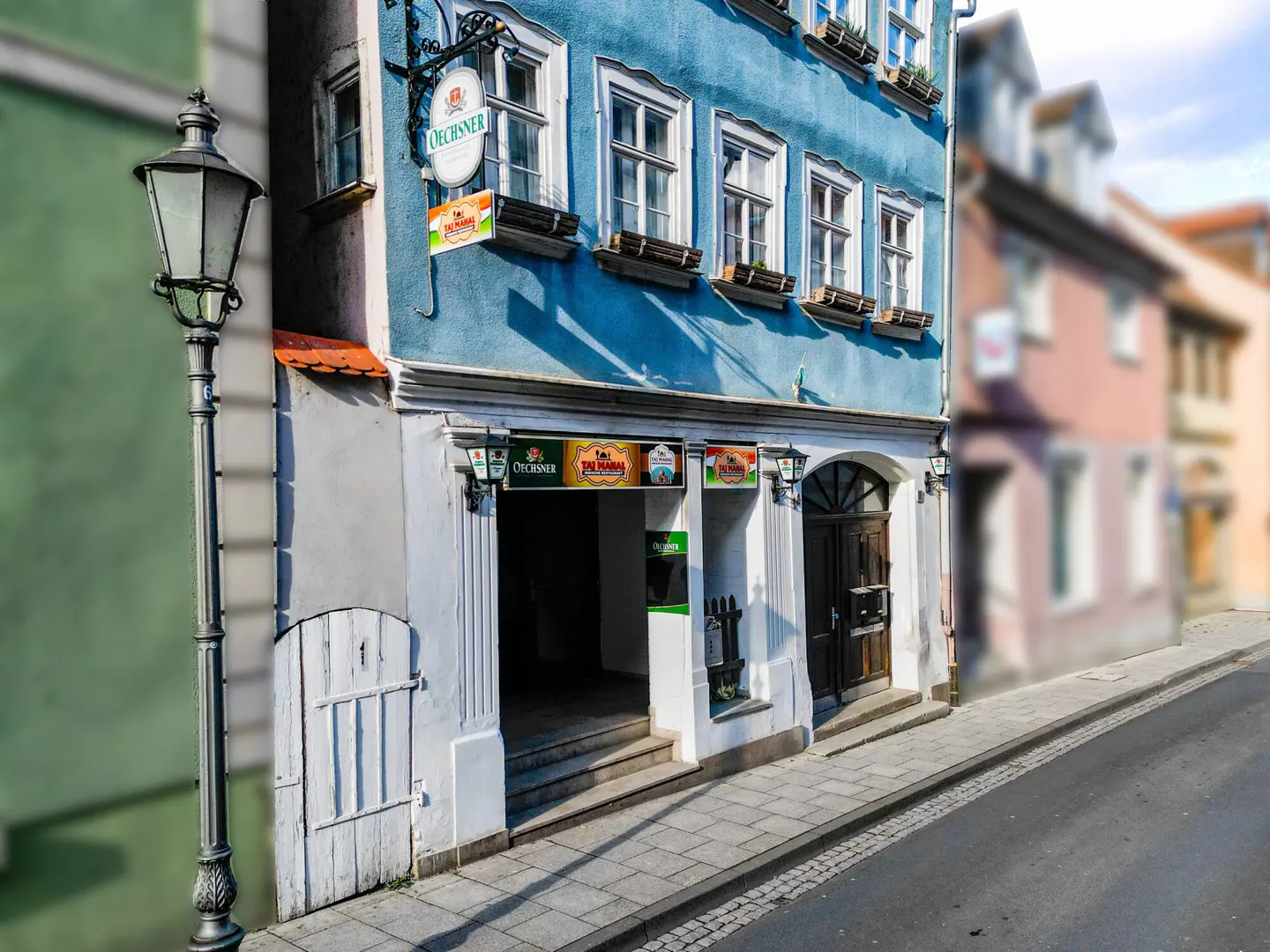 Blue building with white trim and a dark wood door, street lamp on the left, and street in the foreground.