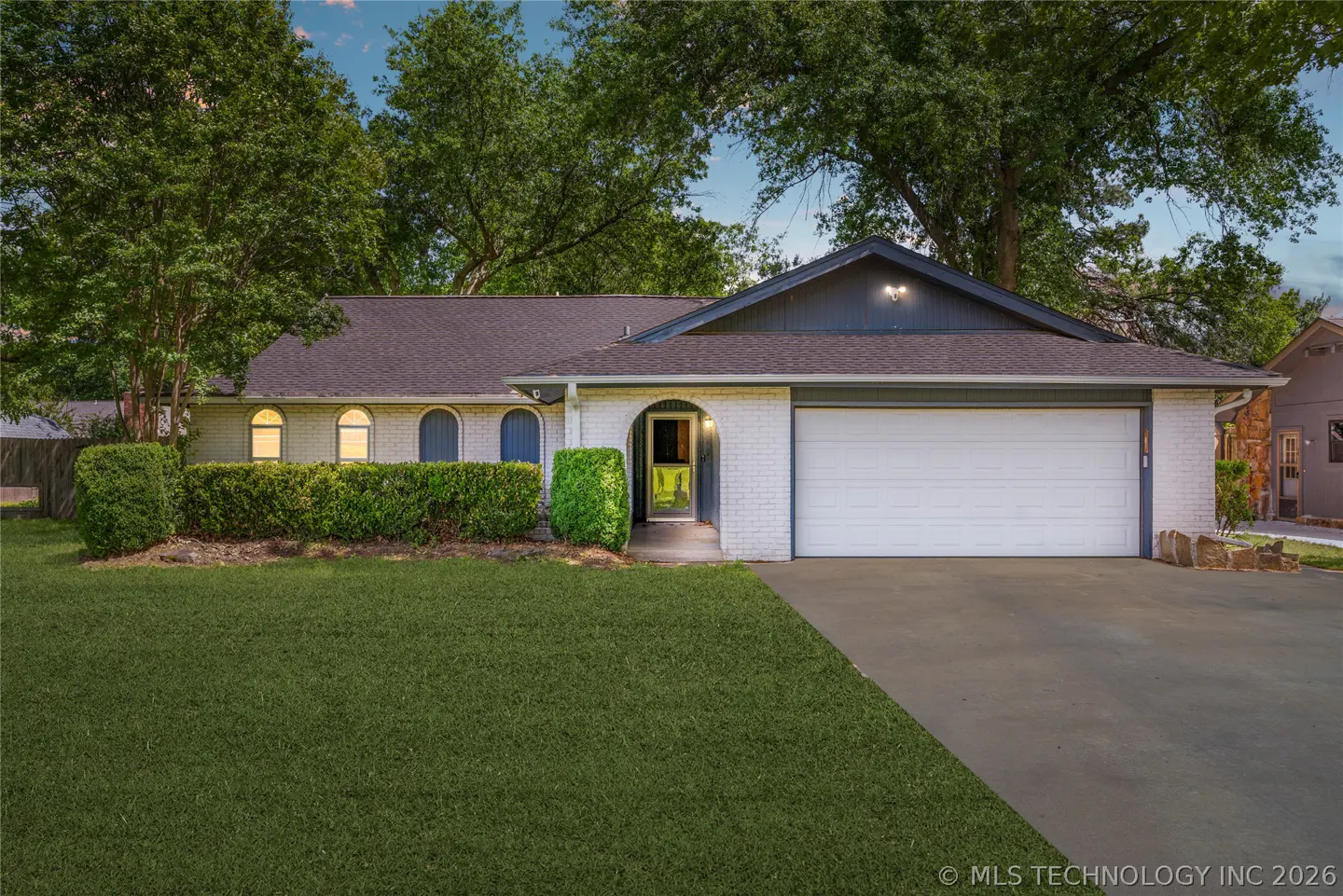 A single-story white brick house with a gray roof, green lawn, and a two-car garage.