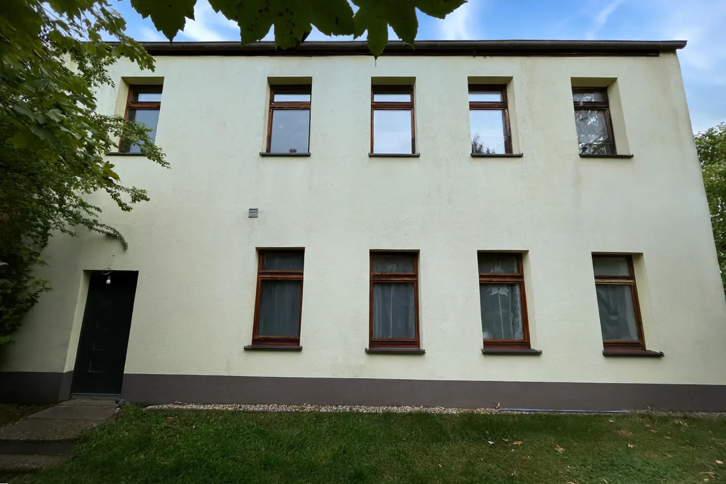 Two-story building with a cream-colored facade, brown trim, and eight windows. A black door is on the left side of the building.