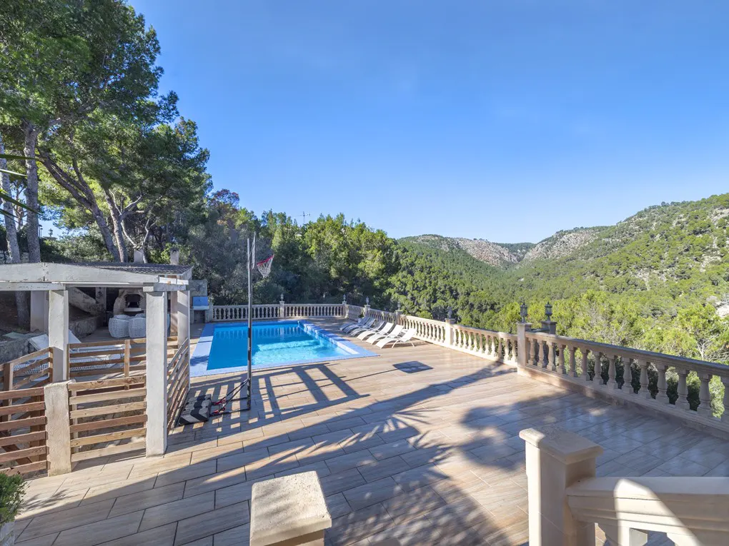 Outdoor pool area with lounge chairs, a basketball hoop, and a view of green hills under a blue sky.
