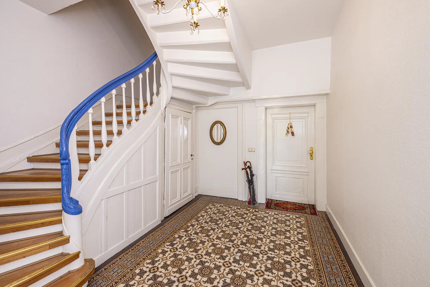 Entryway with patterned tile floor, white staircase with blue handrail, white doors, and an umbrella stand.