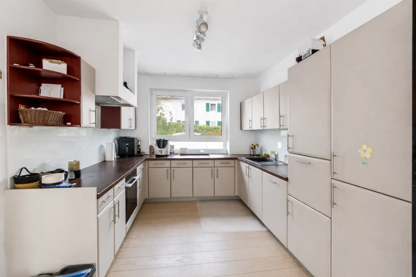 A bright kitchen with white cabinets, dark countertops, and light wood floors. A window overlooks a green yard.