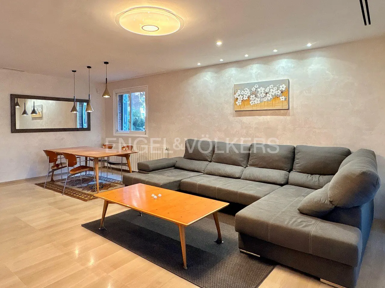 Living room with a gray sectional sofa, wooden coffee table, dining table with chairs, and a mirror on the wall.