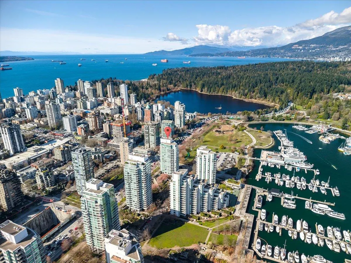 Aerial view of Vancouver, BC, showcasing high-rise buildings, a marina filled with boats, and a backdrop of mountains and ocean.