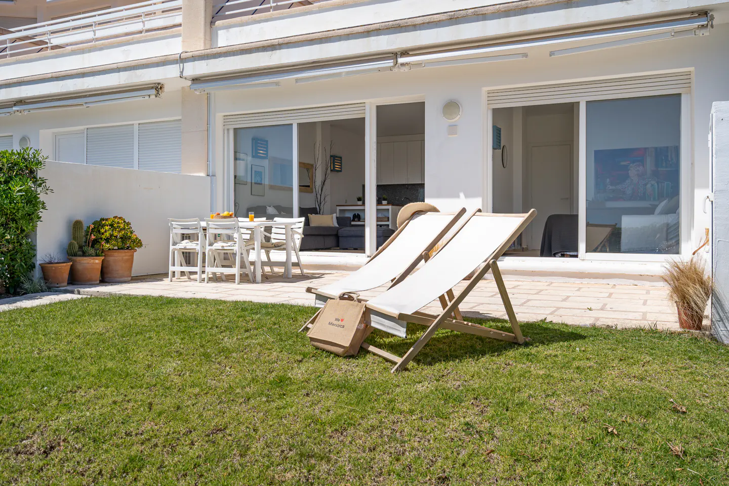 Exterior view of a white building with two lounge chairs on the lawn. A table and chairs are visible on the patio.