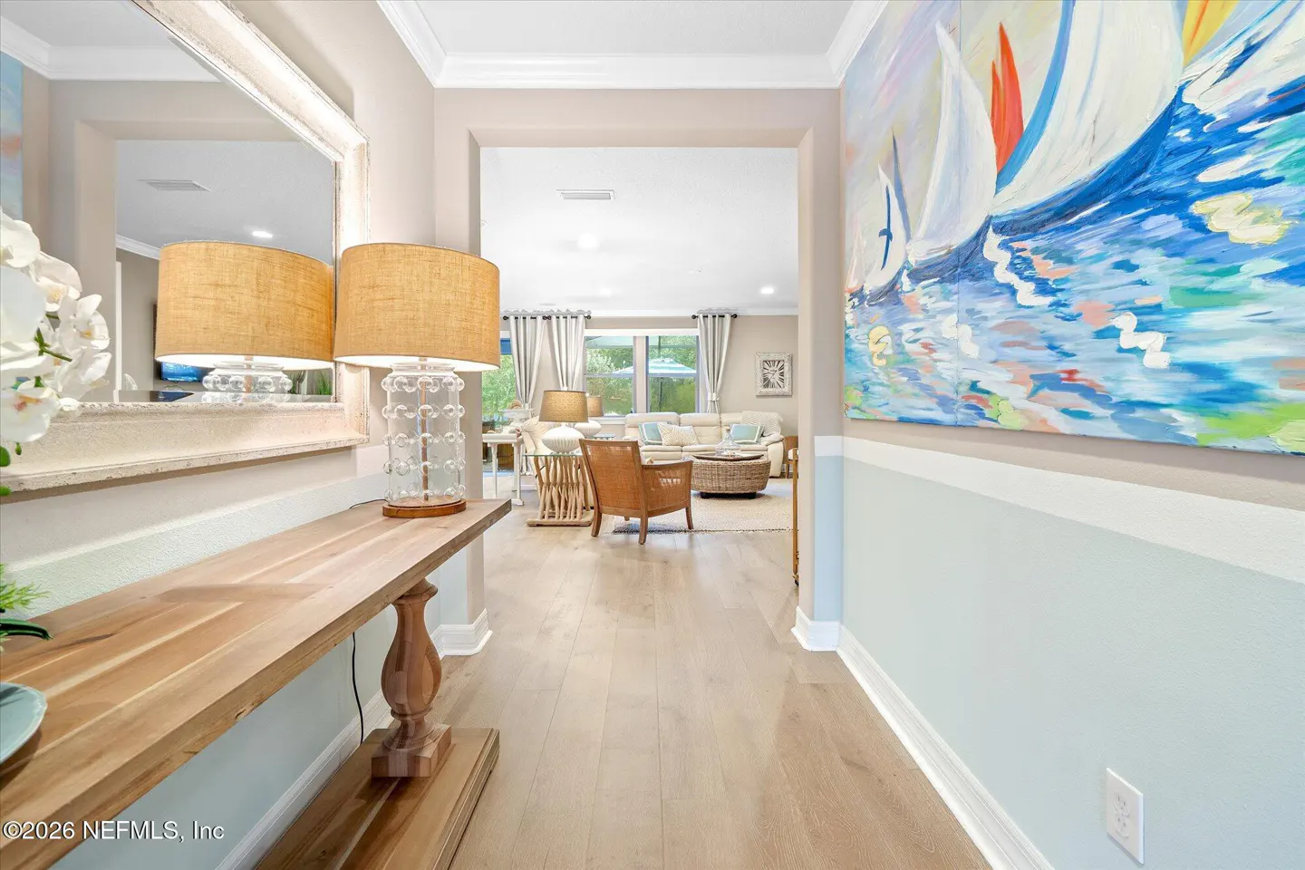 Entryway with a wood console table, glass lamp, and large sailboat painting, leading into a bright, open living room.