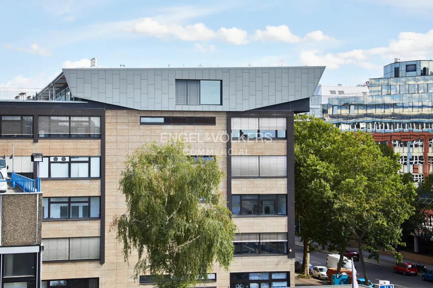 Exterior shot of a commercial building with the Engel & Völkers logo, featuring a modern design with large windows and a light-colored facade.