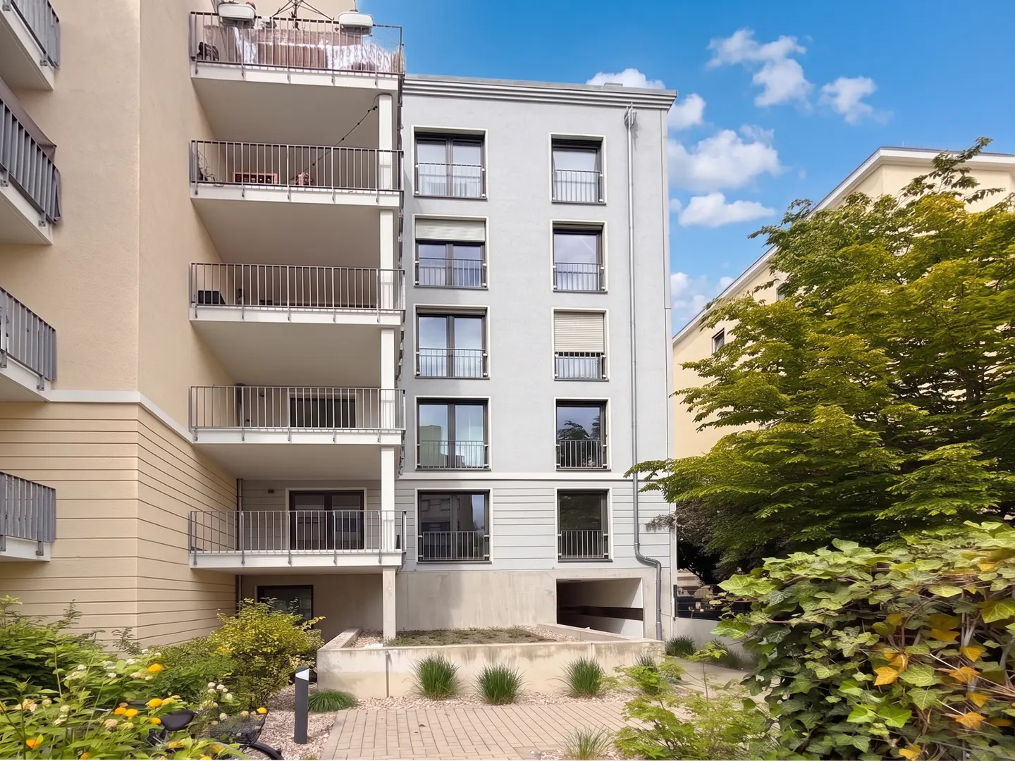 Exterior view of a modern apartment building with balconies, a gray facade, and green landscaping.