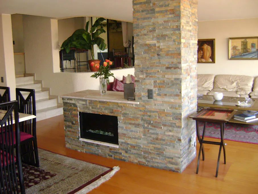 A living room with a stone fireplace, wood floors, and a beige sofa. Art hangs on the wall.