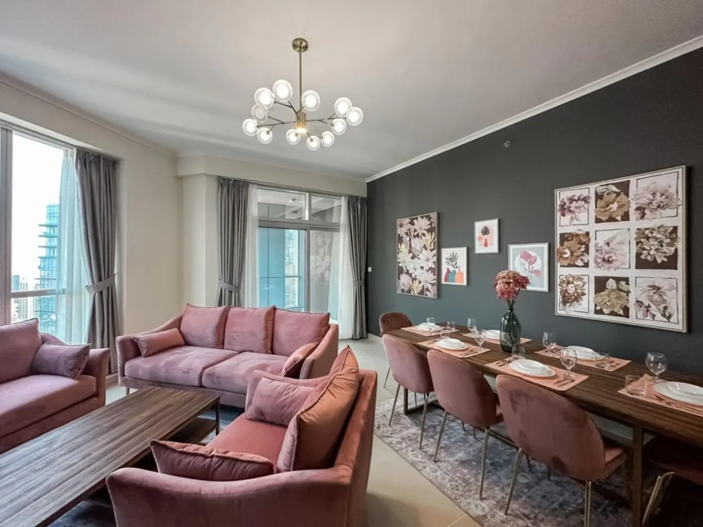 A modern living and dining area with pink sofas, a dark wood table, and city views from large windows.