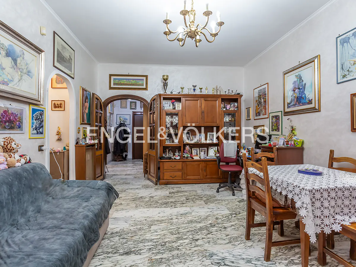 A living room with a gray couch, wooden table and chairs, and a large wooden cabinet filled with decorative items.