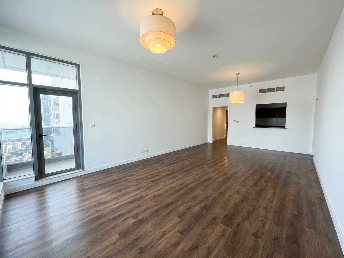 Spacious, empty living room with dark wood-look flooring, white walls, modern pendant lights, and a balcony glass door. [AI-generated text]