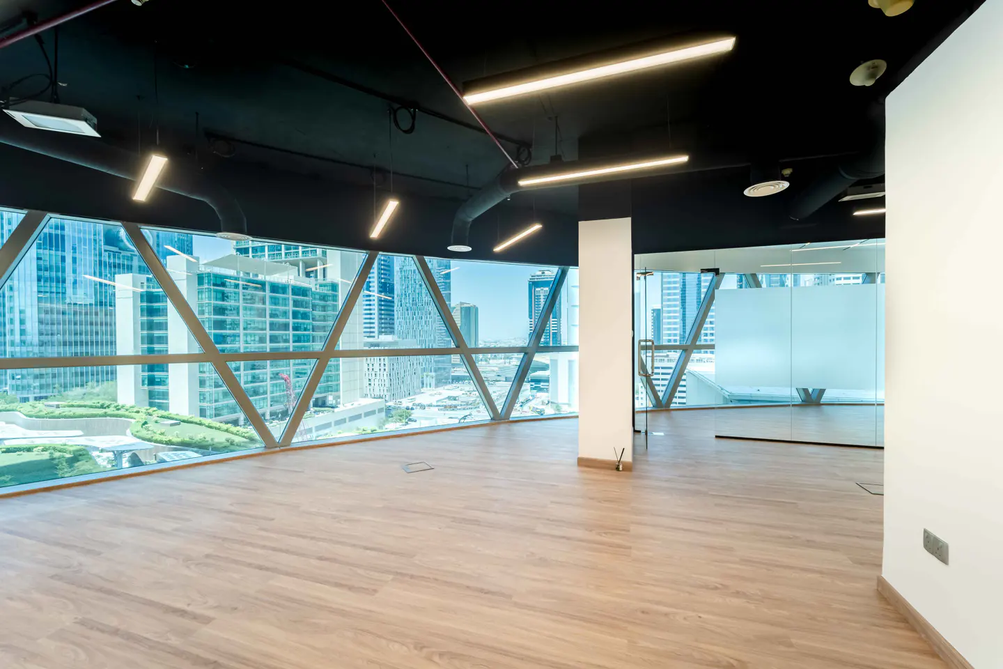 Empty office space with wood floors, black ceiling, and large geometric windows overlooking a city skyline.