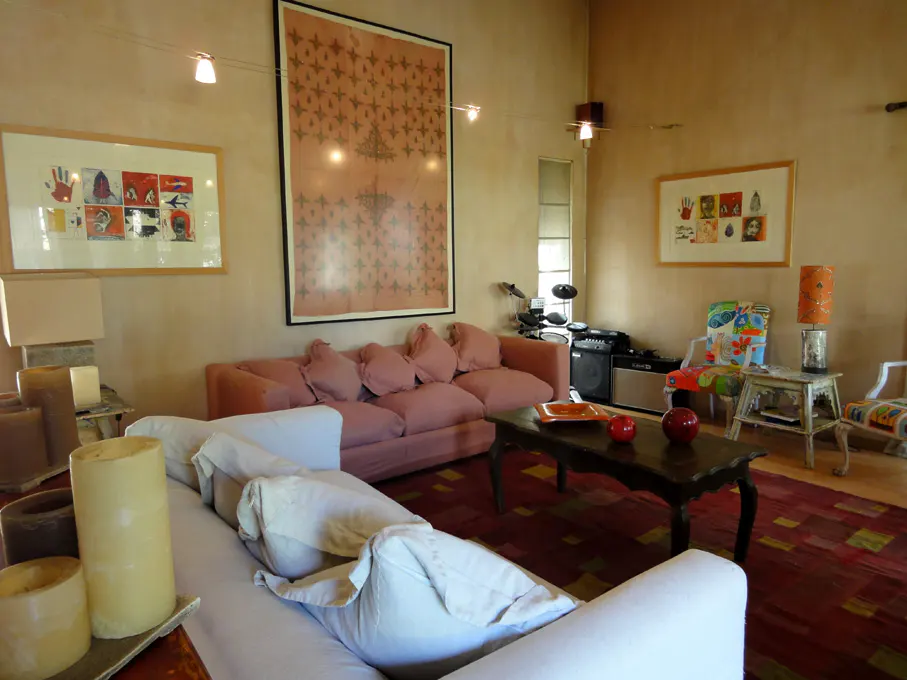 Living room with a pink sofa, white sofa, dark wood coffee table, and artwork on the walls. A drum set is visible in the background.