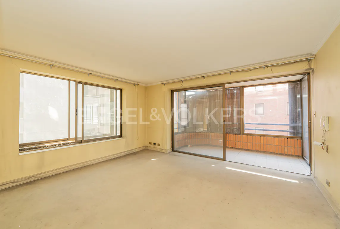 Empty room with beige walls, a large window, and sliding glass doors to a balcony with brick railing.