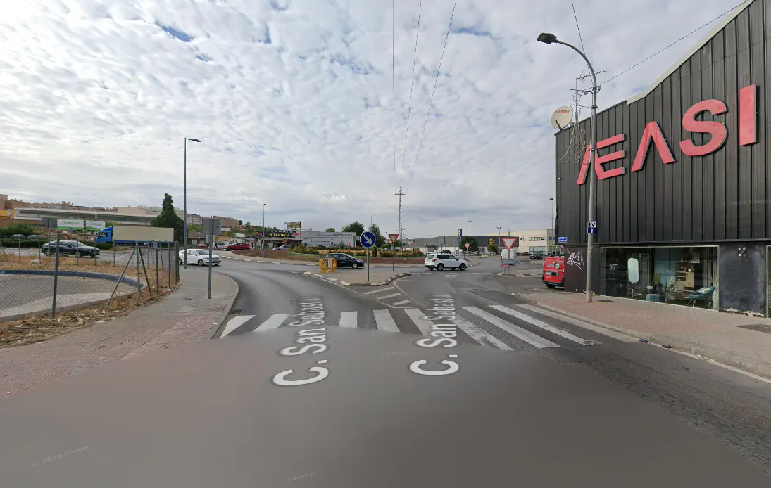 Street view of a road intersection with crosswalks, a roundabout, and a large black building with red lettering.