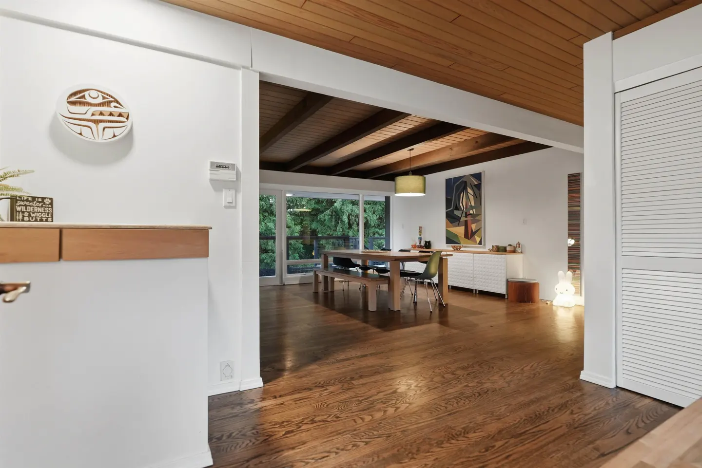 A bright, open-concept dining room with wood floors and a wood-paneled ceiling. A table and chairs sit near sliding glass doors.
