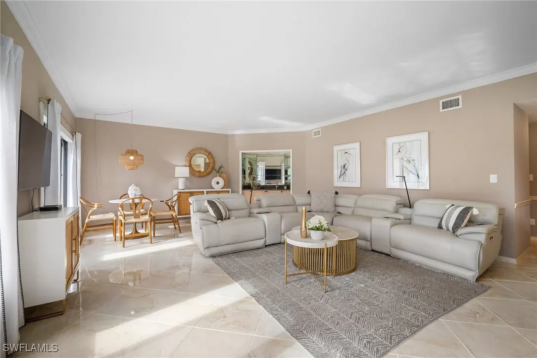 A living room with beige walls, a large gray sectional sofa, a round table, and a dining area with a round table and chairs.