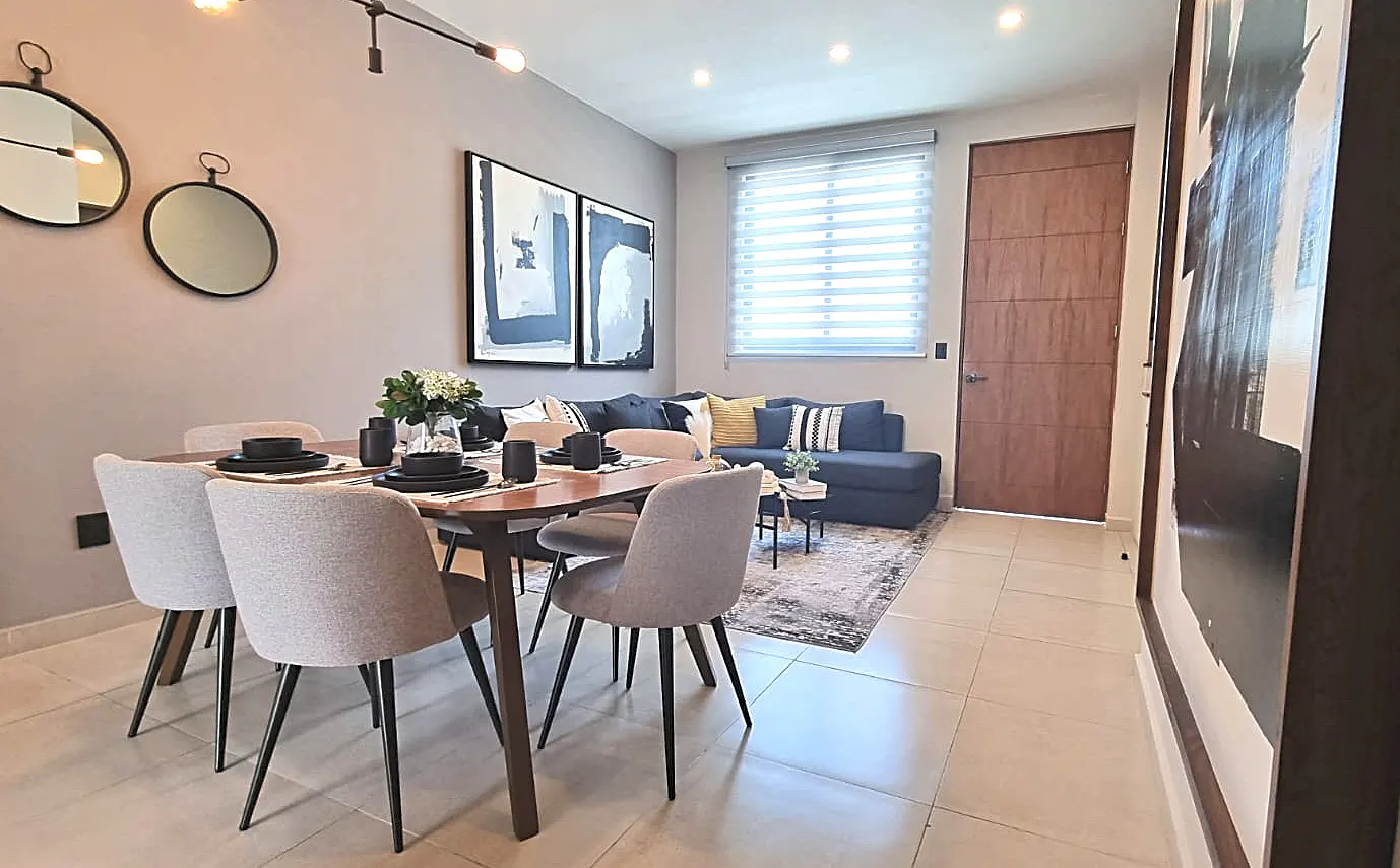 A modern dining and living room with a wooden table, gray chairs, and a blue sofa with decorative pillows.