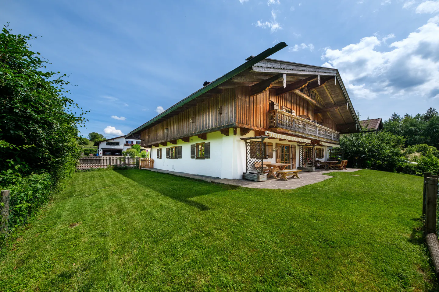 Traditional Alpine-style house with white walls, wooden upper level, and a stone patio in a lush green backyard.