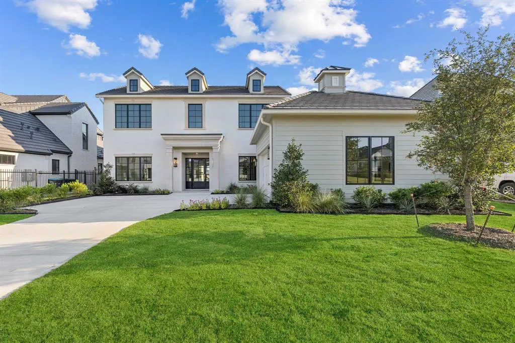A two-story white house with black window frames, a green lawn, and a concrete driveway under a blue sky.