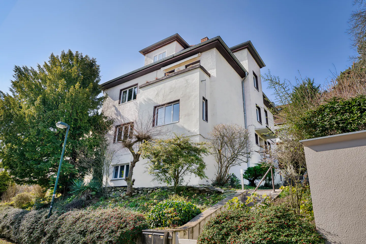 A three-story white building with brown trim sits on a green, sloping lawn under a blue sky.