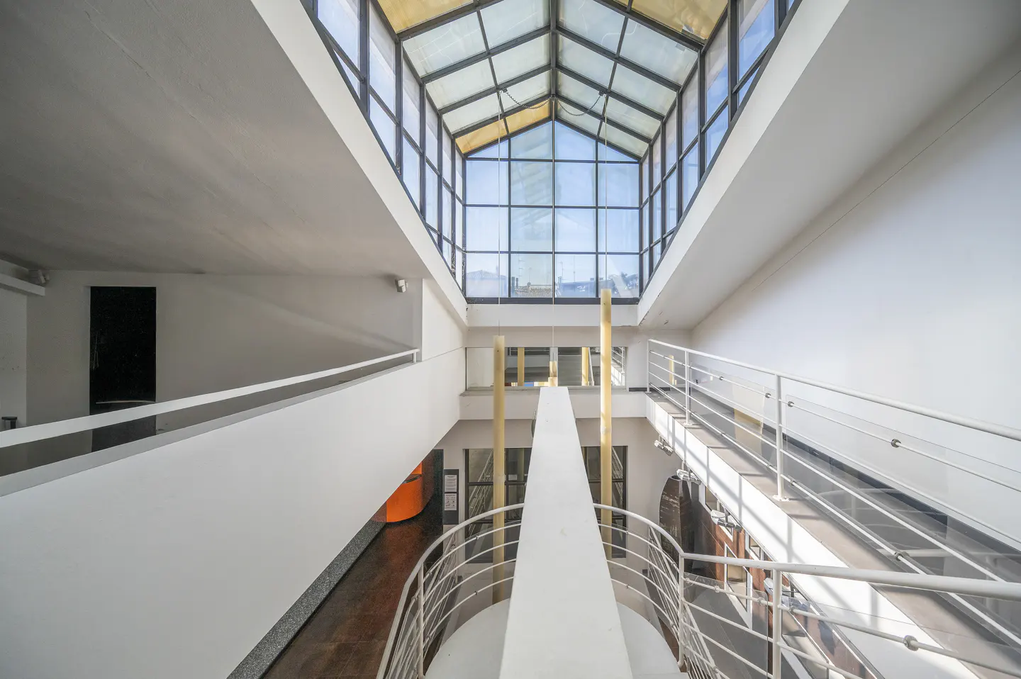 Interior view of a modern building with white walls, a glass ceiling, and metal railings.