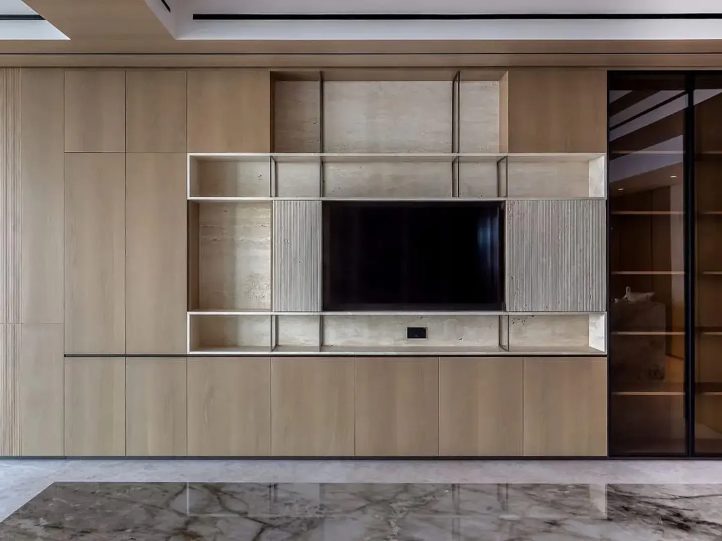 Modern light wood media wall with built-in shelving, a central flat-screen TV, and a glass-fronted display cabinet.