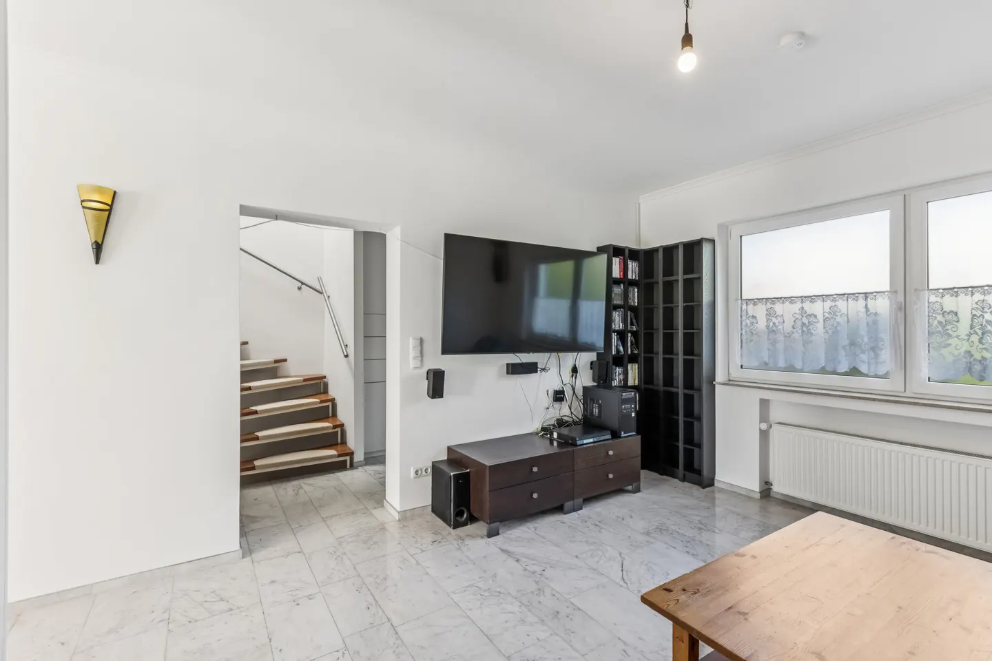 Living room with marble floors, white walls, a TV, and a staircase in the background.
