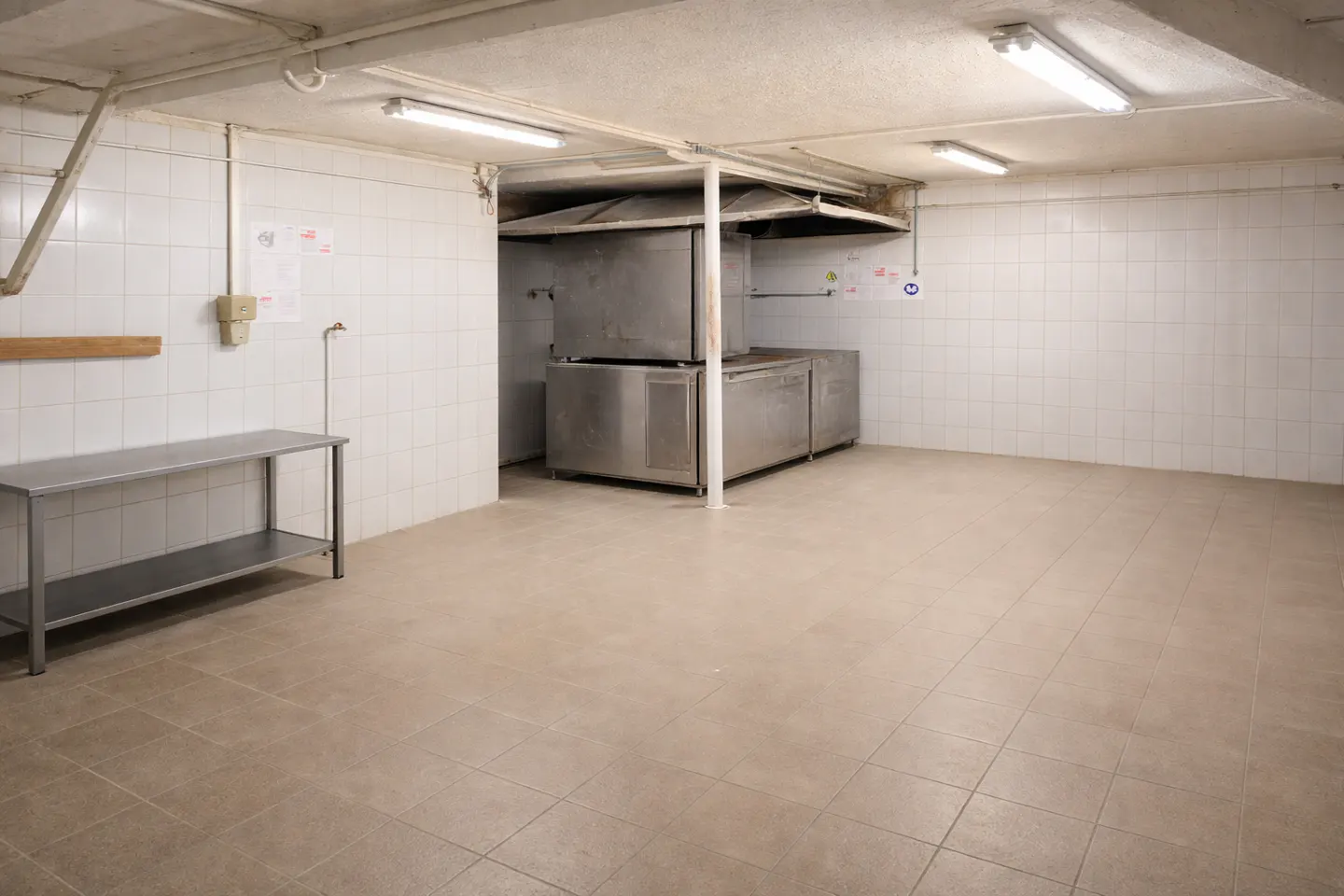 A commercial kitchen with stainless steel appliances, white tiled walls, and a metal table.