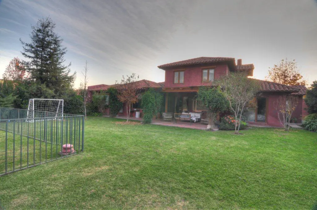 A red house with a tile roof overlooks a green lawn with a soccer goal and fence.