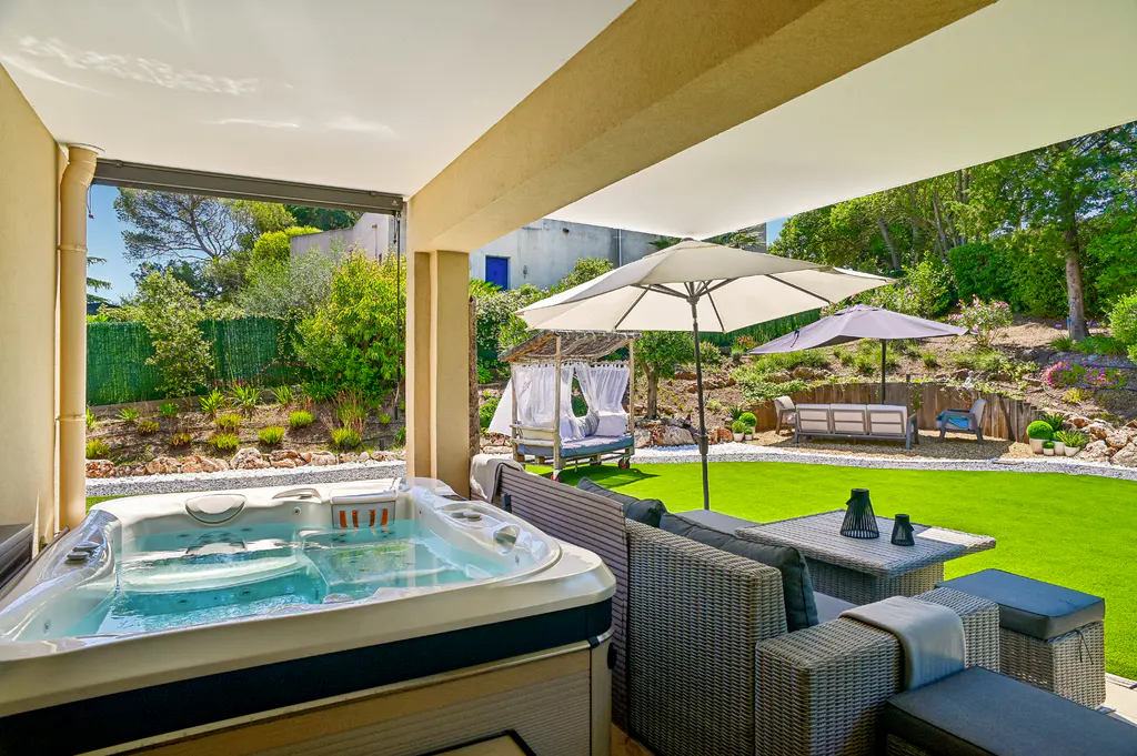 Outdoor patio with a hot tub, wicker furniture, and a green lawn with lounge chairs and umbrellas.